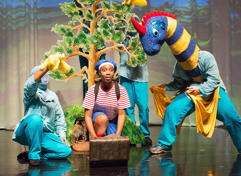 Elmer, wearing a blue beret and his knapsack, sits with the yellow and blue striped dragon puppet in Enchantment Theatre Company's "My Father's Dragon."