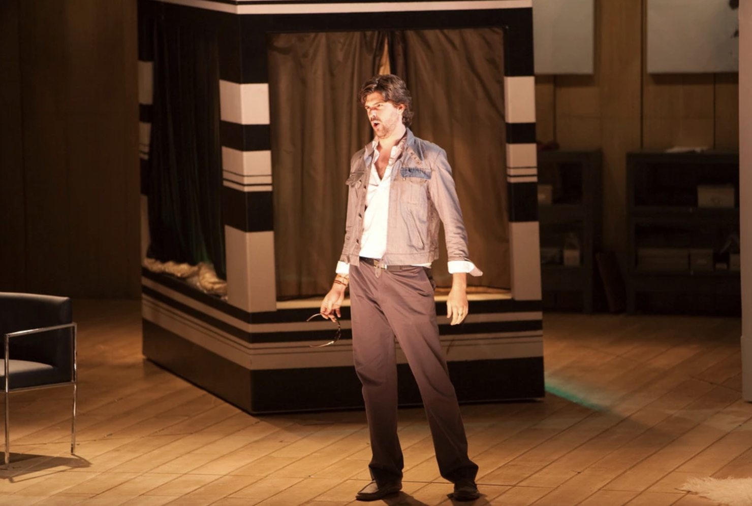 Tenor Zach Borichevsky, a bearded man with wavy brown hair in a white shirt, khaki jacket, and brown pants and shoes, sings on the set of a Gianni Schicchi production.