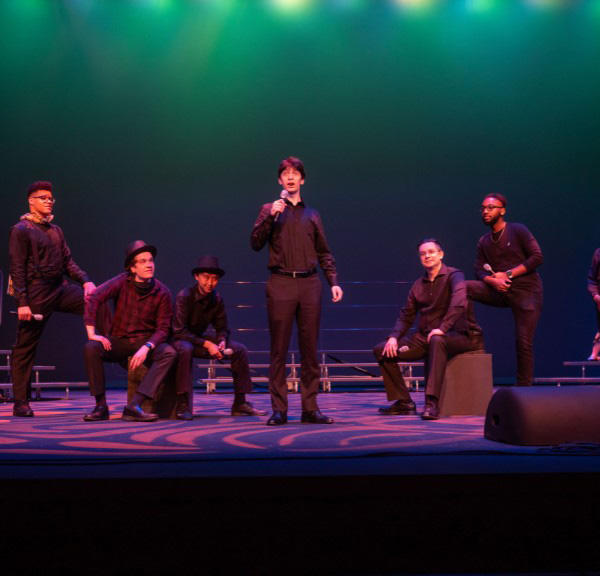 students dressed in black, sitting and standing and singing on stage