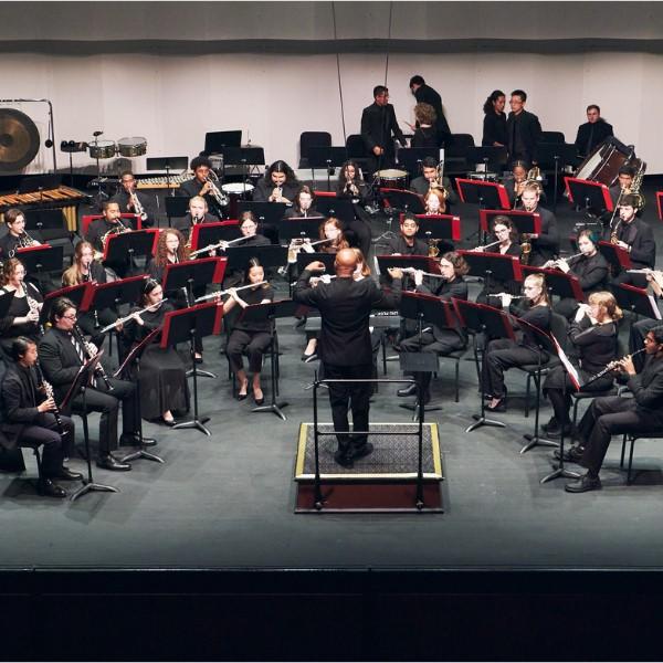 Wind Symphony - group of people dressed in black, sitting playing instruments with man in front of them conducting