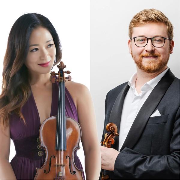 Woman in a purple dress holding a violin and man in a suit holding a violin