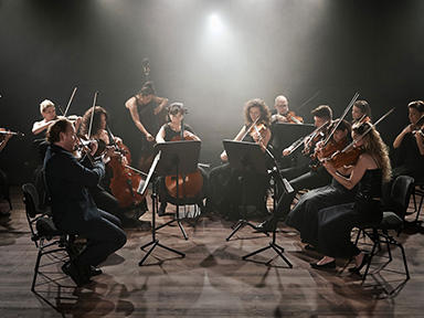 Zurich Chamber Orchestra string players perform seated onstage, under a hazy light..