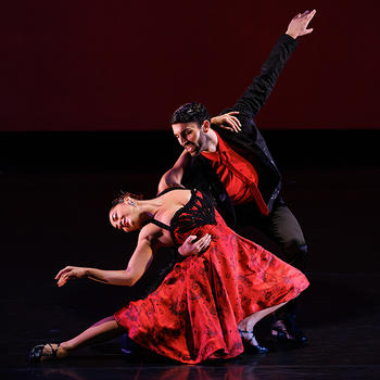 Both wearing red and black, a male Ballet Hispanico dancer dips a female dancer, who leans back with arm outstretched.